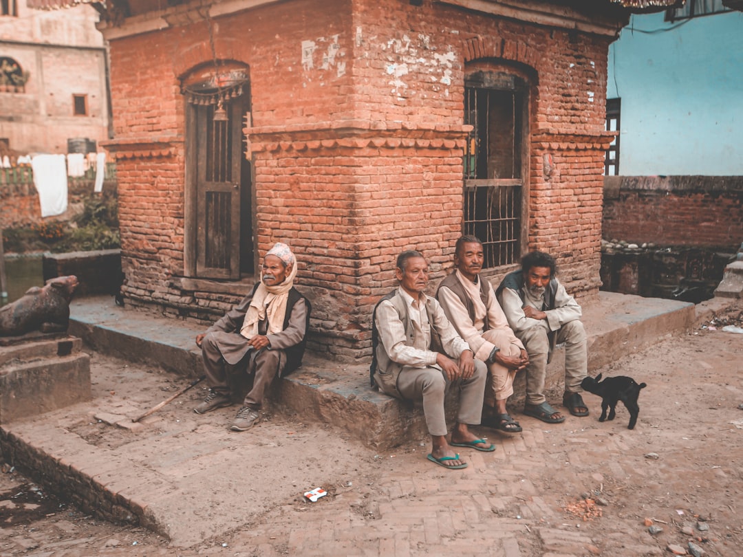 3 men sitting on concrete bench near brown brick building during daytime