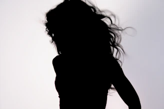 An elegant silhouette of a woman with flowing hair, embodying grace and mystery against a soft pastel background.
