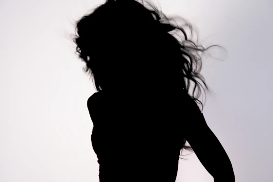An elegant silhouette of a woman with flowing hair, embodying grace and mystery against a soft pastel background.