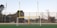 A football field with a goalpost featuring both a soccer goal and an American football uprights. An American flag is visible to the left, and trees are visible in the background. The ground is covered with artificial turf.
