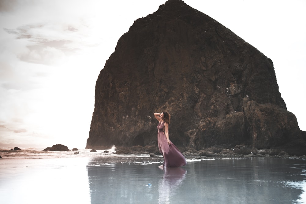 woman in green dress standing on rock formation near body of water during daytime