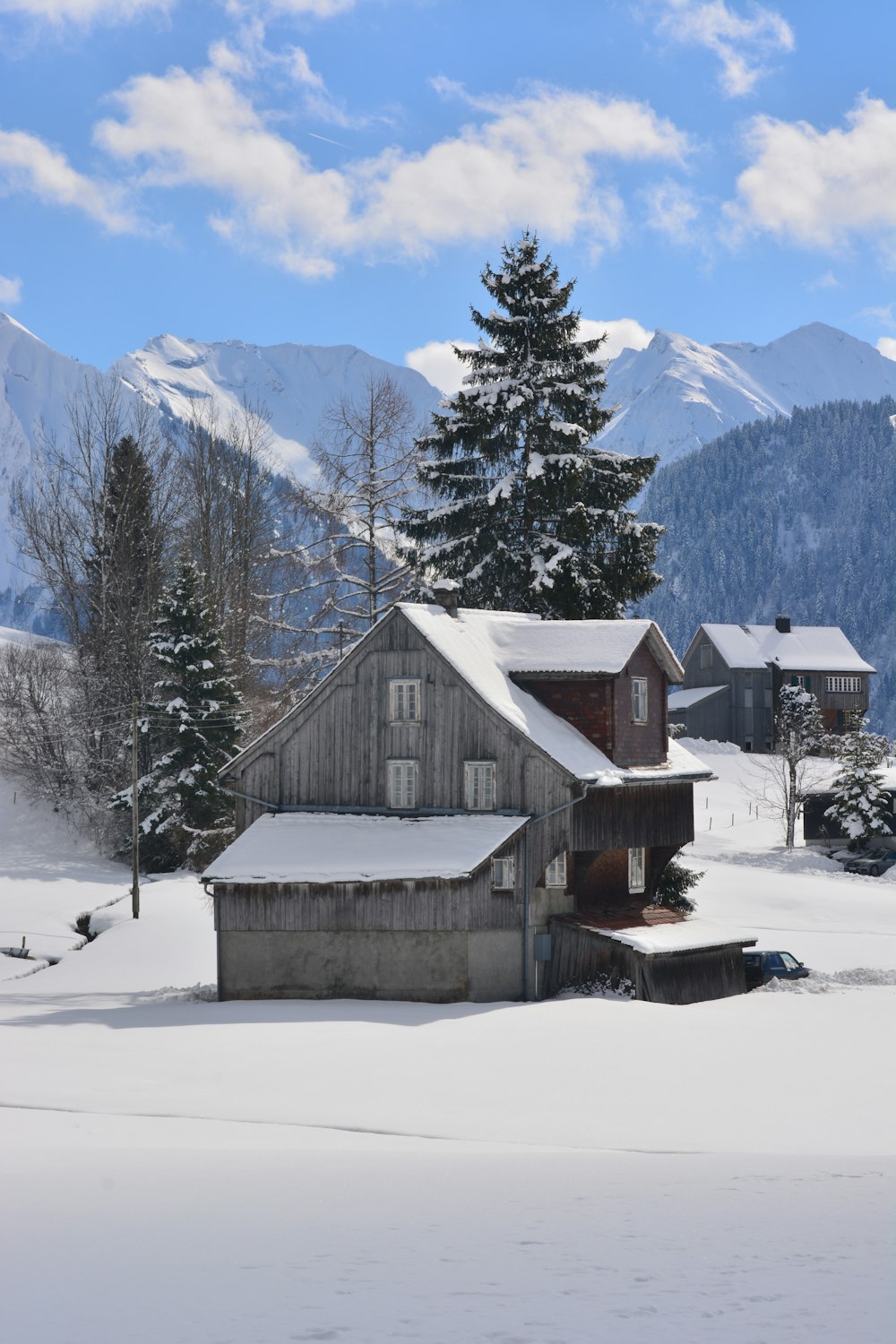 brown wooden house on snow covered ground near green trees and snow covered mountains during daytime