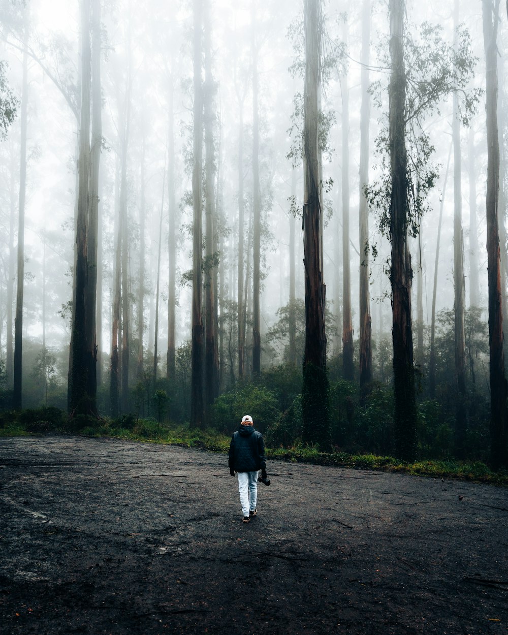man in black jacket walking on pathway between trees
