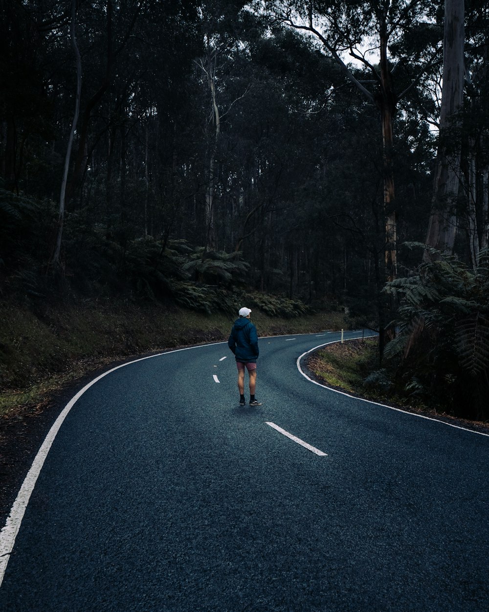 man in black jacket and blue denim jeans walking on road during daytime