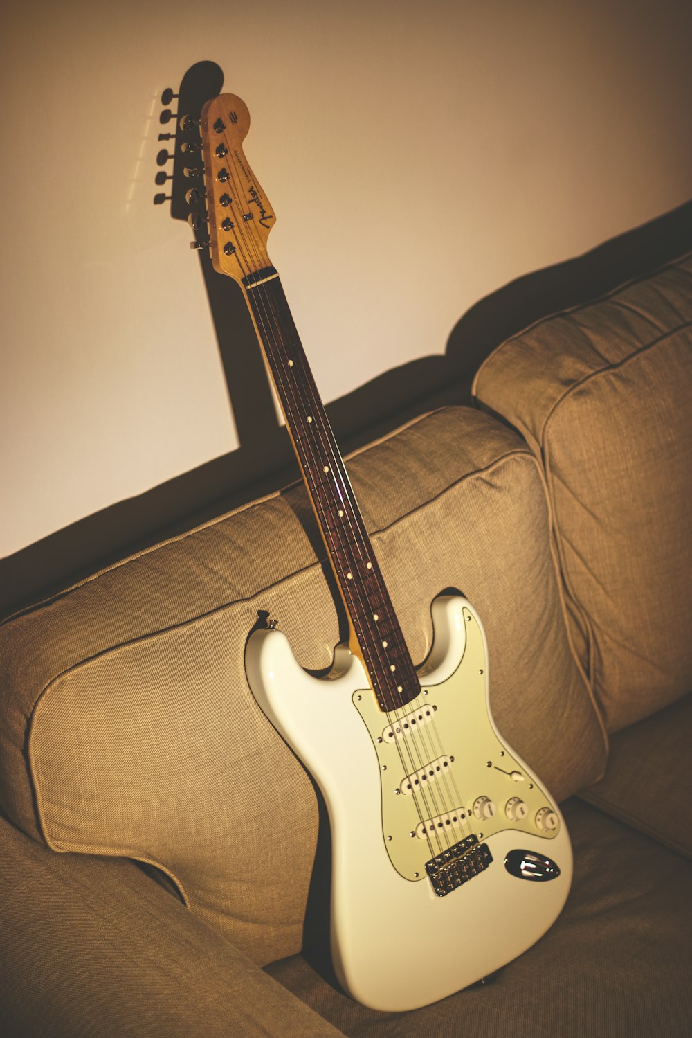 white and black stratocaster electric guitar on brown sofa