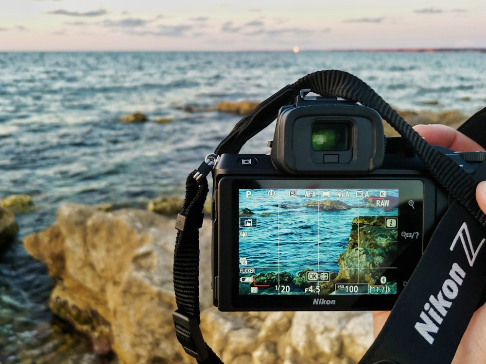 日中に海岸に打ち寄せる海の波の写真を撮る黒いサムスンデジタル一眼レフカメラ