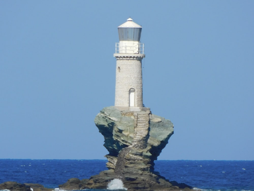 Weißer und brauner Leuchtturm auf brauner Felsformation in der Nähe des Meeres tagsüber