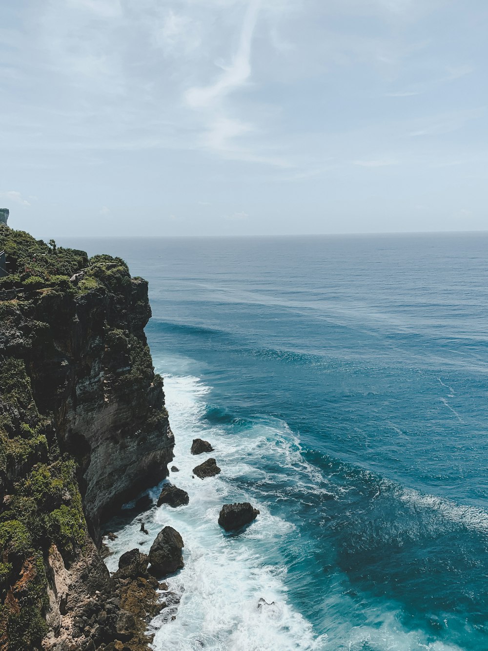 green and brown rock formation beside blue sea under white clouds during daytime