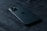 A sleek, modern smartphone with a triple camera setup is lying on a dark textured surface. The phone appears to be made of reflective material and is positioned slightly diagonally.