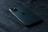 A sleek, modern smartphone with a triple camera setup is lying on a dark textured surface. The phone appears to be made of reflective material and is positioned slightly diagonally.