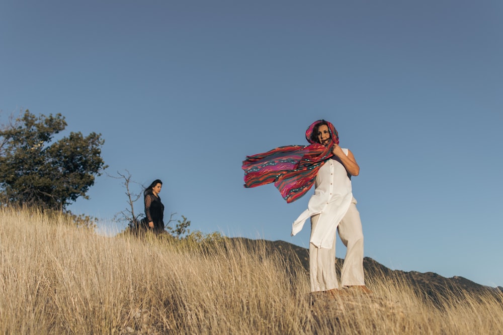 woman in white long sleeve shirt and red scarf standing on brown grass field during daytime