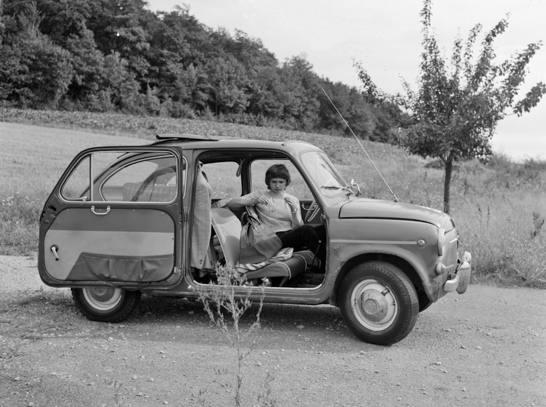 grayscale photo of man and woman sitting on car hood