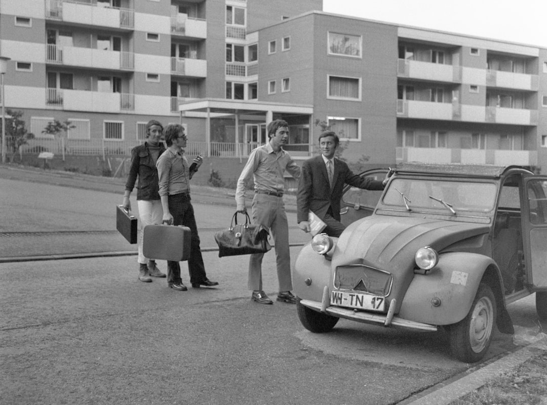 grayscale photo of couple standing beside classic car