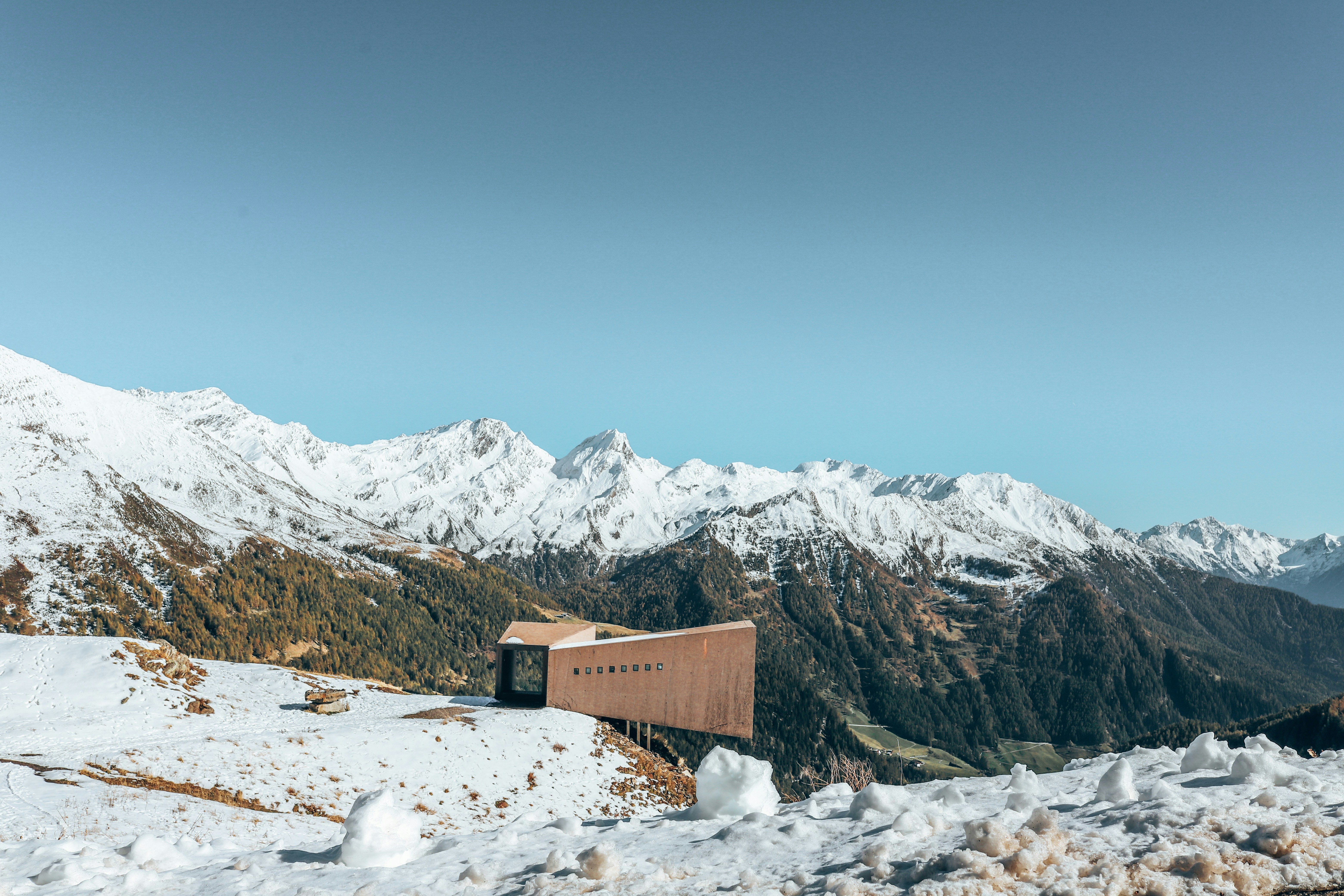 brown wooden house on snow covered ground near snow covered mountain during daytime