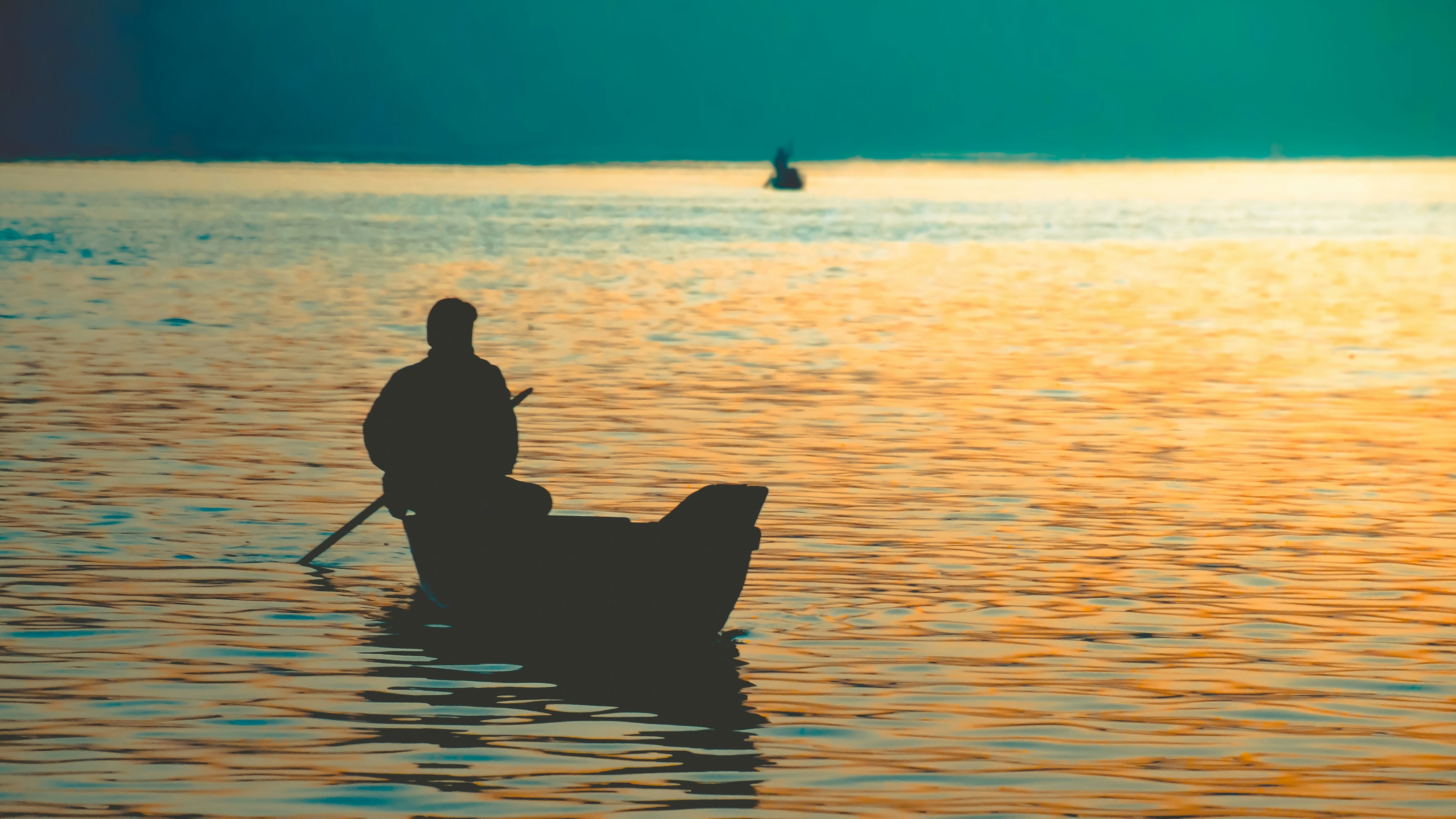 silhouette of man riding boat on sea during sunset