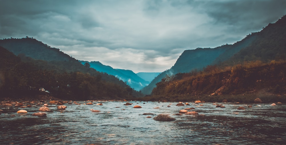 body of water near mountains under cloudy sky during daytime