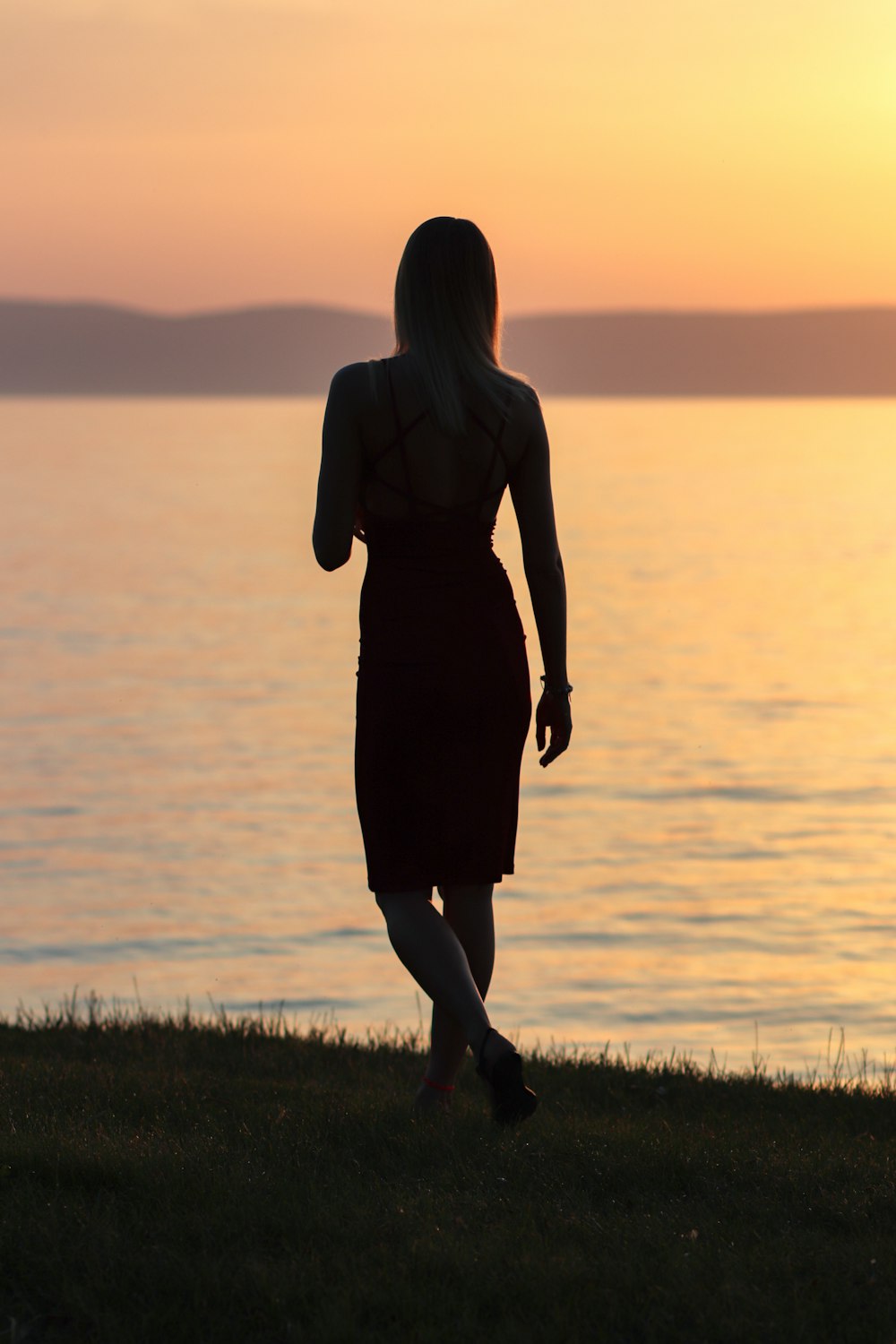 woman in black dress standing on green grass field during sunset