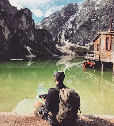 man in brown jacket sitting on brown rock near body of water during daytime