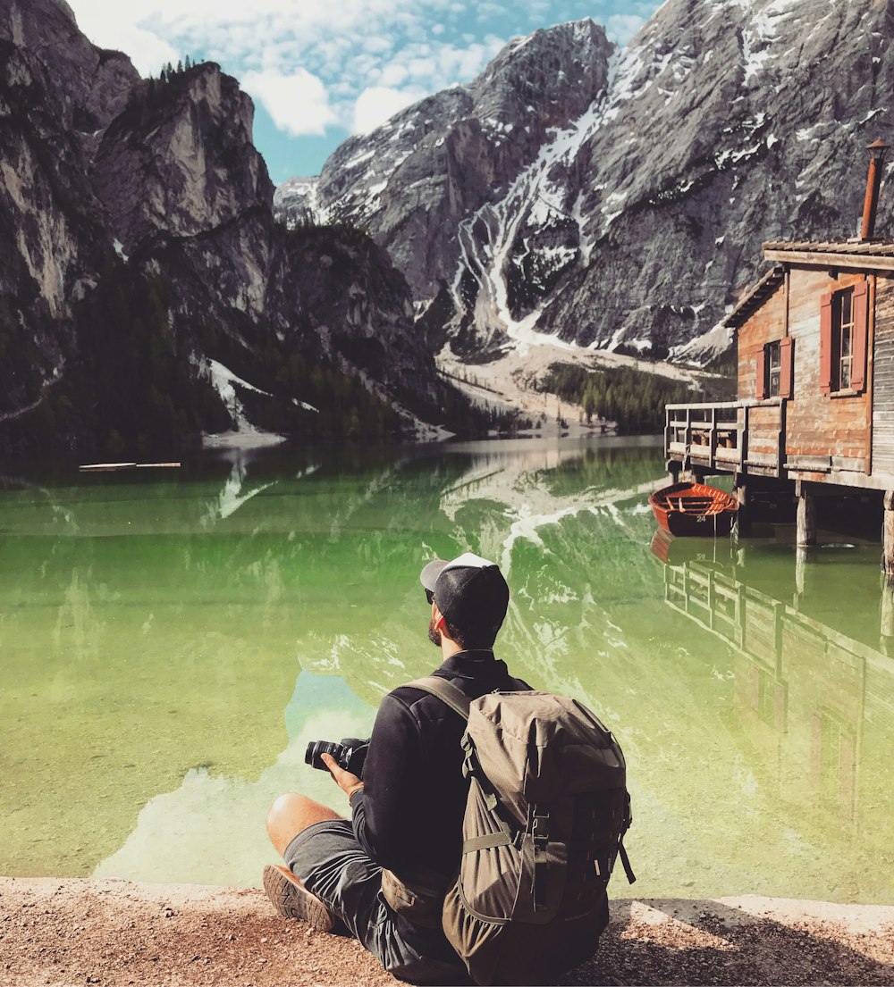 man in brown jacket sitting on brown rock near body of water during daytime