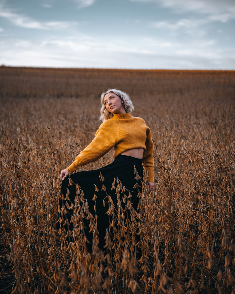 woman in yellow long sleeve shirt and black and white floral skirt standing on brown grass