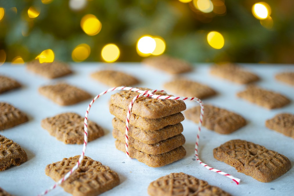 Pile de spéculoos ficelée d’un fil rouge et blanc, entourée d’autres biscuits devant des lumières de fête (photo d’illustration)