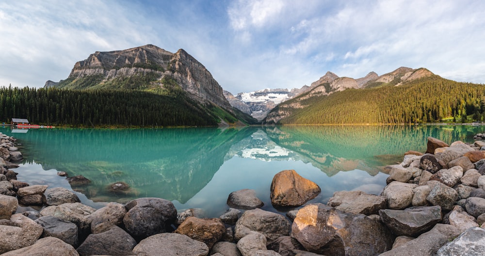 montanhas verdes e marrons ao lado do lago sob o céu azul durante o dia