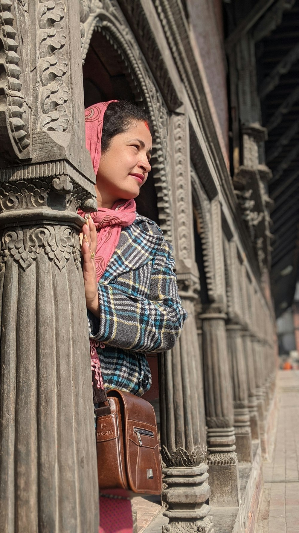 woman in red white and black plaid dress shirt standing near brown concrete post during daytime