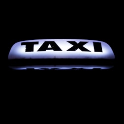 A bright, illuminated taxi sign against a dark background, featuring bold black lettering that stands out sharply.