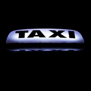 A bright, illuminated taxi sign against a dark background, featuring bold black lettering that stands out sharply.