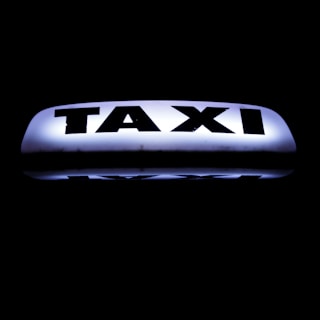 A bright, illuminated taxi sign against a dark background, featuring bold black lettering that stands out sharply.
