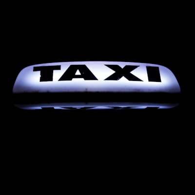 A bright, illuminated taxi sign against a dark background, featuring bold black lettering that stands out sharply.
