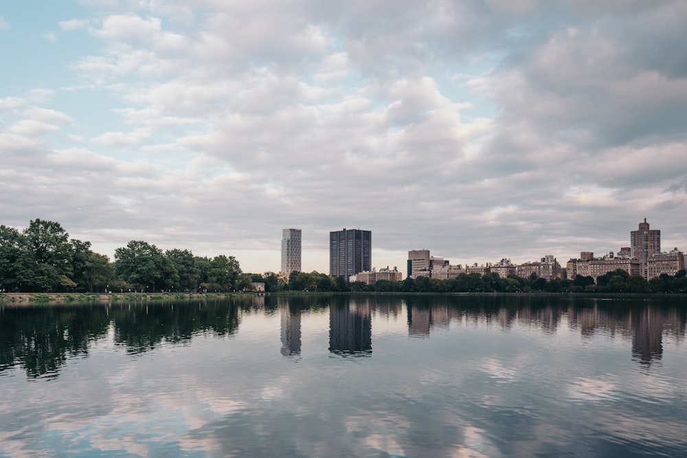 body of water near trees and buildings under cloudy sky during daytime