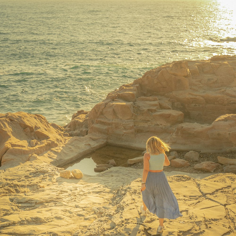 woman in white dress sitting on brown rock near body of water during daytime