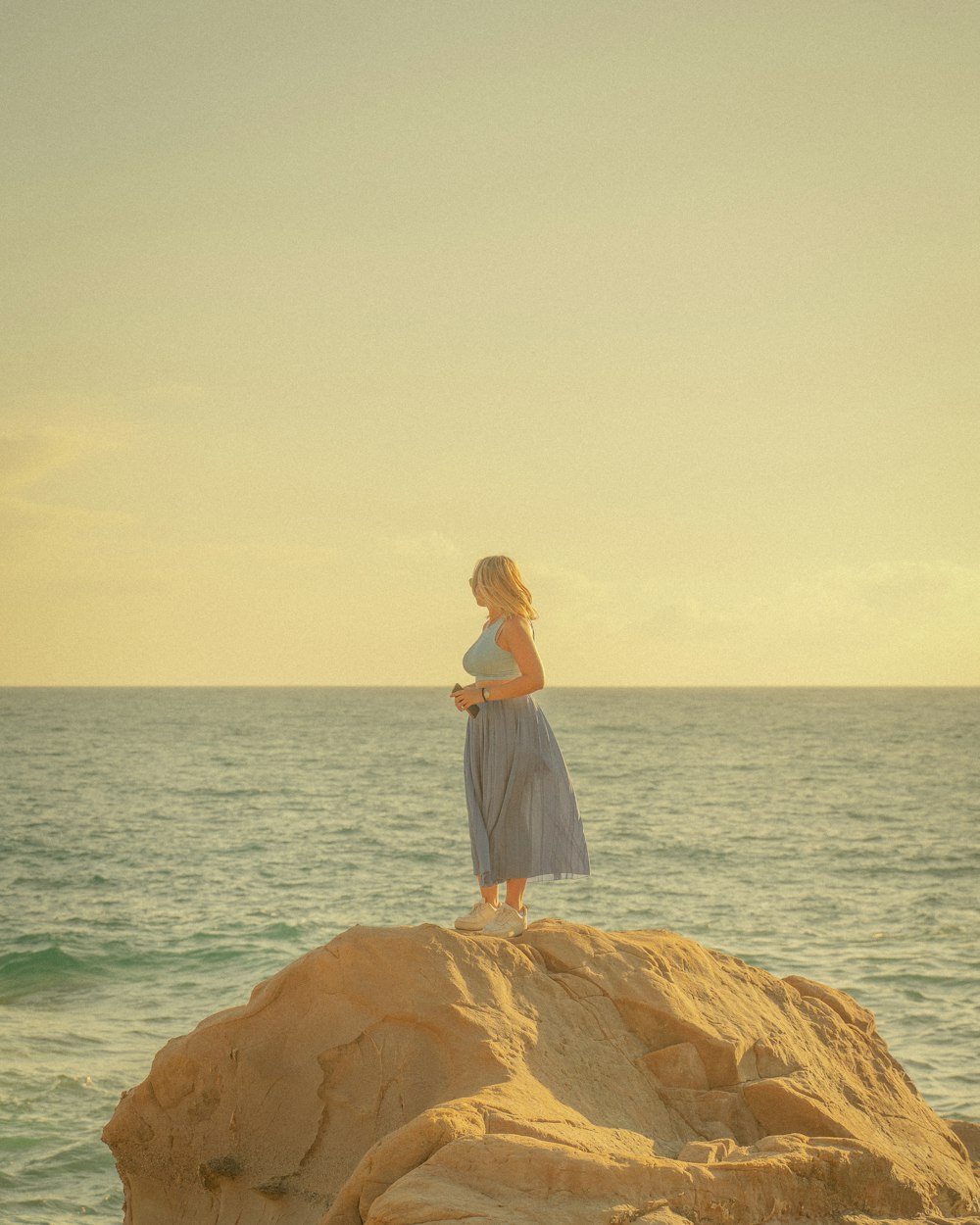 woman in white dress standing on brown rock formation near body of water during daytime