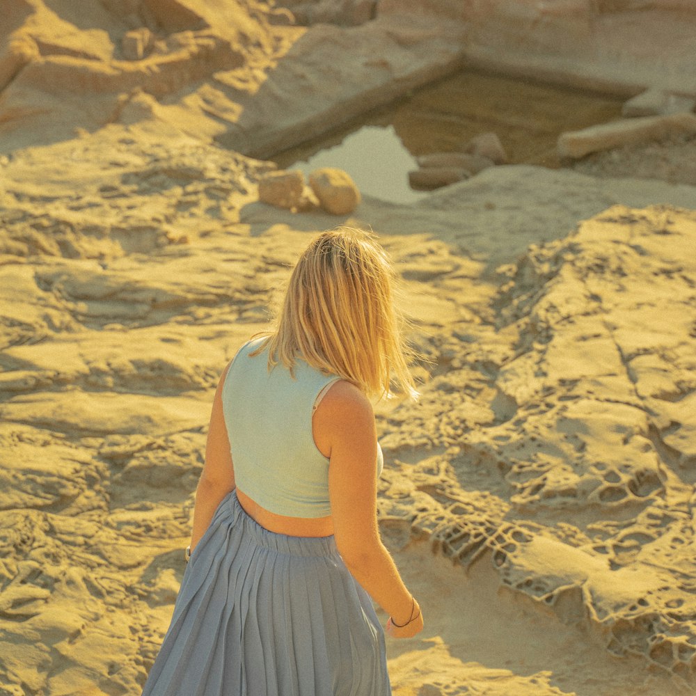 woman in white tank top and blue skirt standing on sand