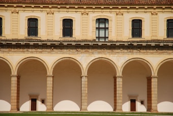 A symmetrical architectural structure featuring a series of arches supported by columns. Above the arches are detailed stone carvings and a row of large rectangular windows. The building has a classical aesthetic with its beige color and intricate design.