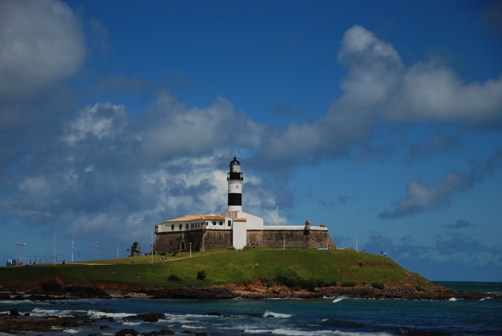 white and black lighthouse on green grass field under blue sky during daytime