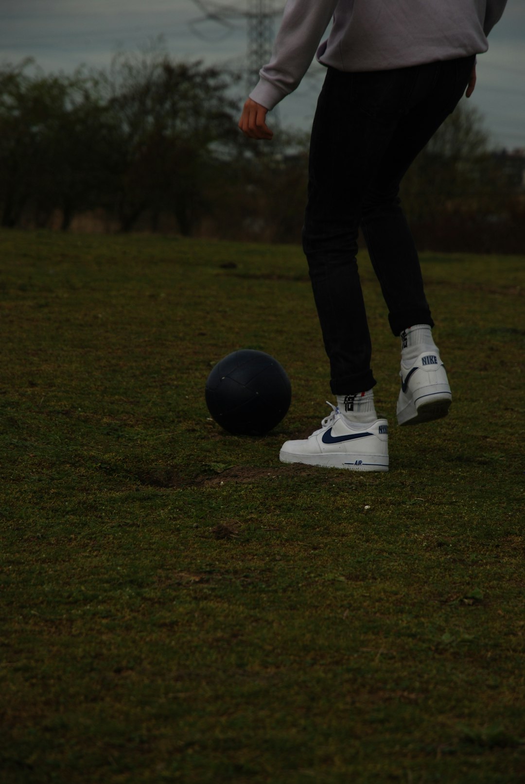 person in black pants and white nike sneakers standing on green grass field