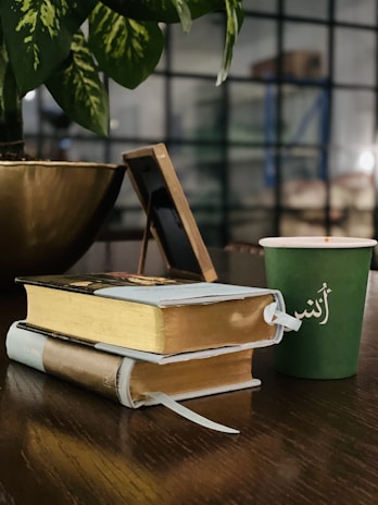 A serene desk with an open Qur’an, a notebook with Arabic calligraphy, and a cup of tea by a window.