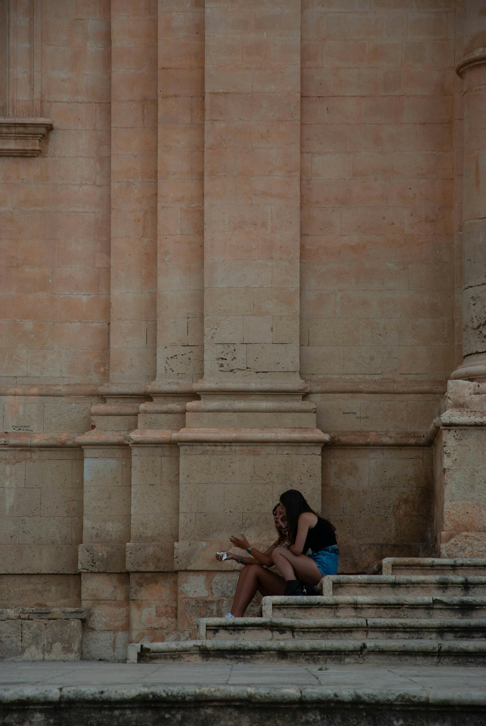 uomo e donna che si siedono sulla panchina vicino all'edificio in cemento marrone durante il giorno