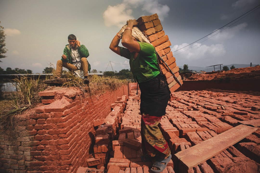 man in green t-shirt and black shorts standing on brown brick wall during daytime