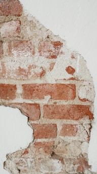 Exposed brick wall with patches of mortar visible, partially covered by white plaster. The texture of the bricks and mortar gives a rough, aged appearance.