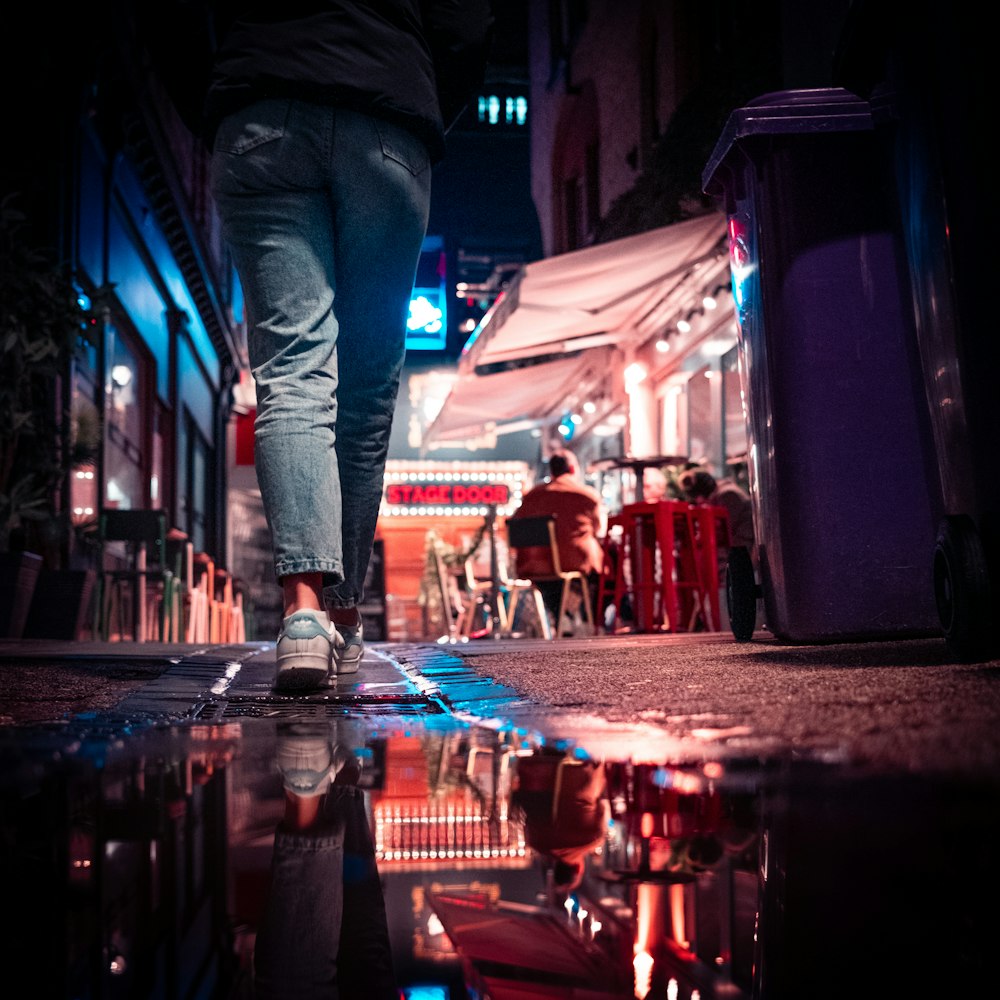 man in blue denim jeans standing on street during nighttime