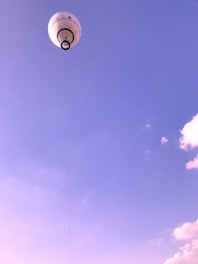 A large tethered balloon floats high in the sky, connected by a cable. The sky is clear with a few clouds scattered around, predominantly showing shades of blue and purple.