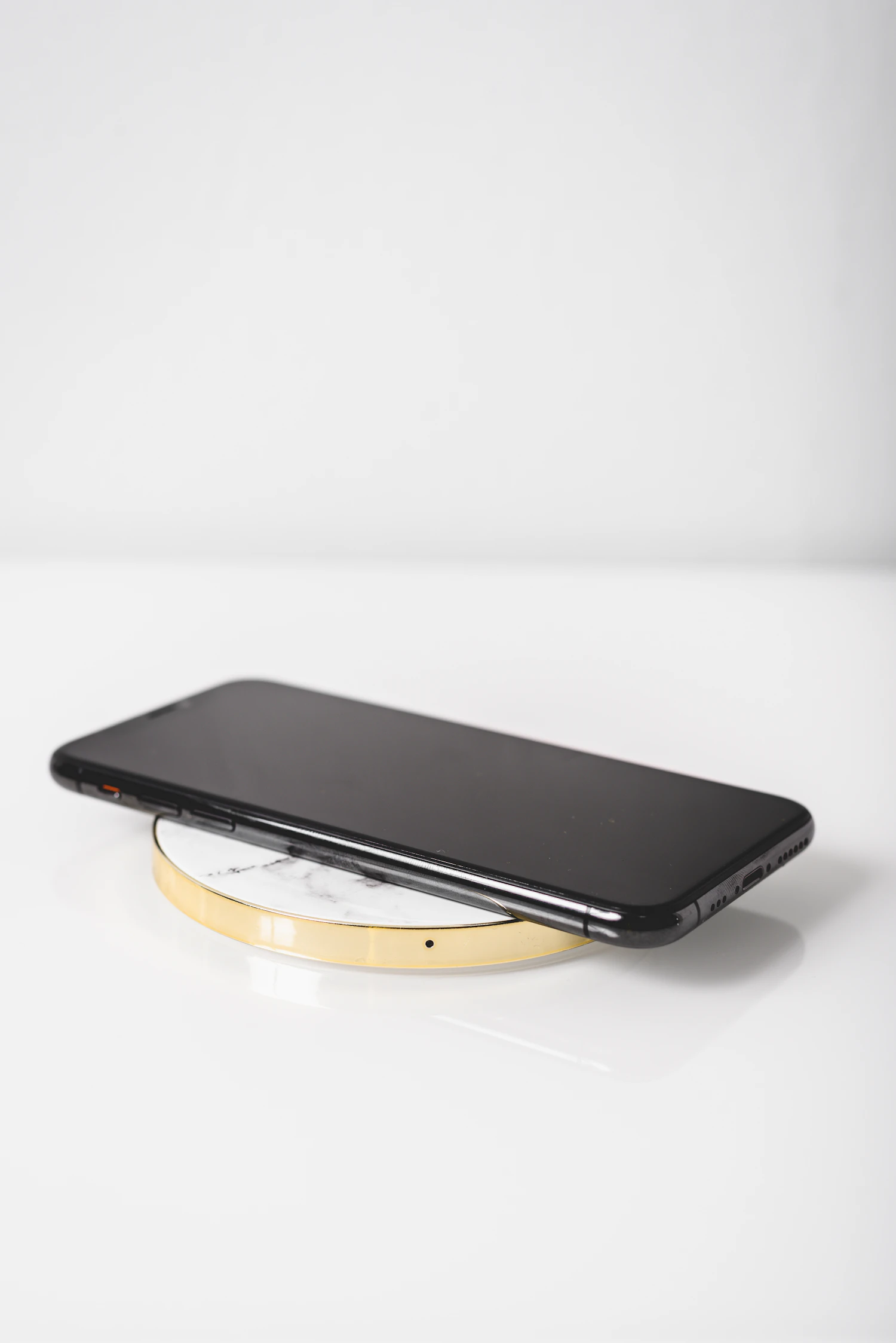 A black phone resting on a round charging pad on a white shelf