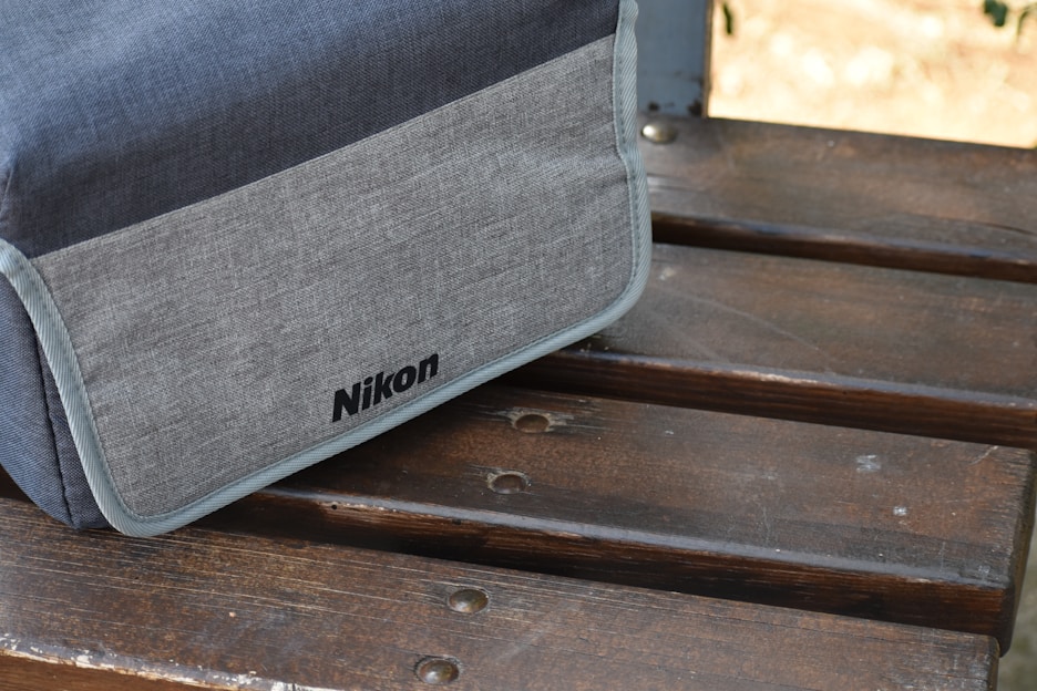 A sleek camera bag resting on a wooden bench with a vintage camera peeking out under warm natural light.