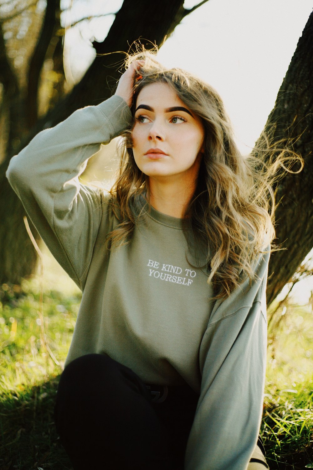 woman in gray long sleeve shirt standing near brown tree during daytime