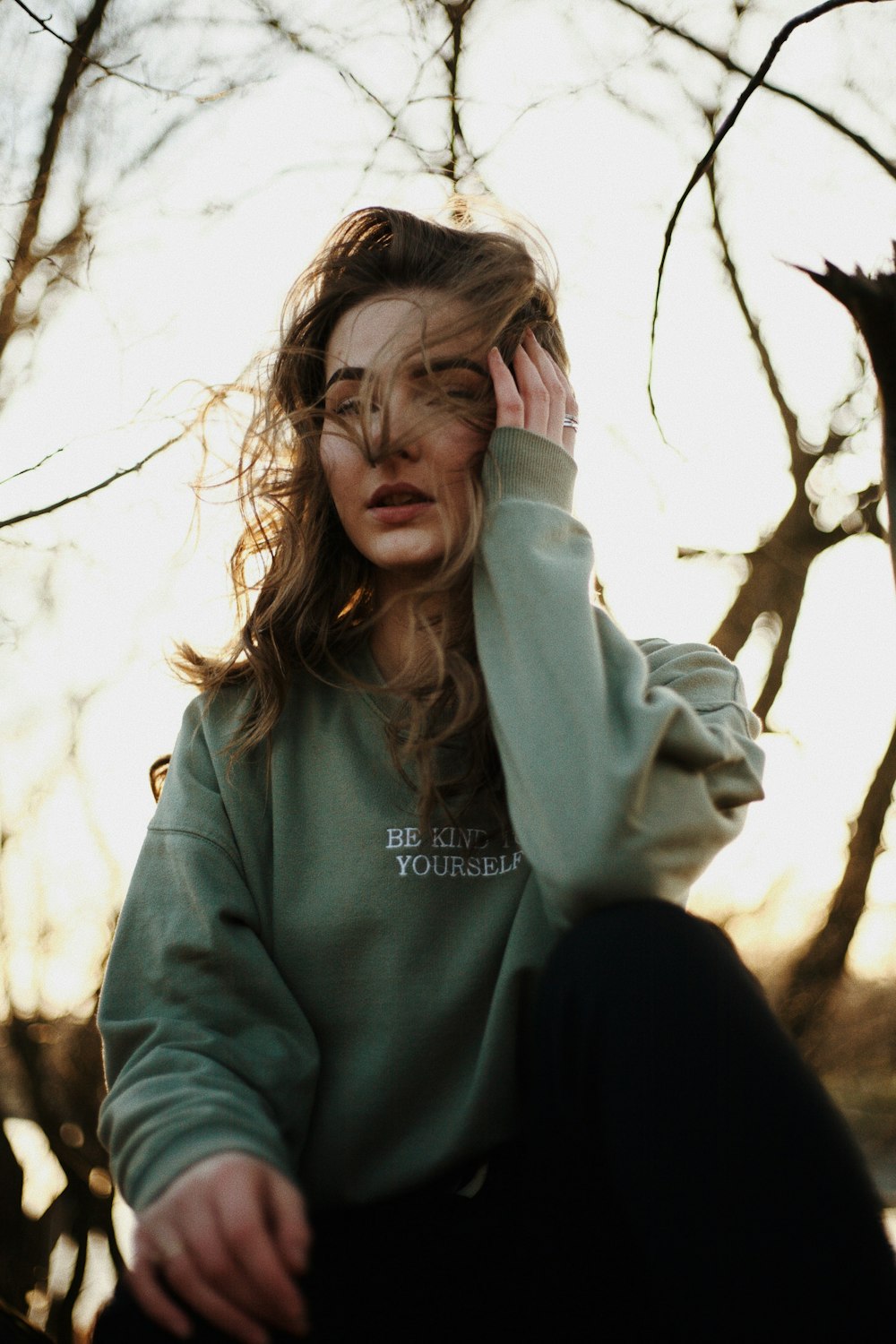 woman in gray hoodie standing near bare tree during daytime