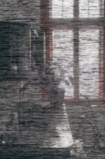 A grainy and distorted image featuring a faint outline of a window casting dim light on a textured surface. The scene is obscured by horizontal noise lines, creating an abstract appearance.