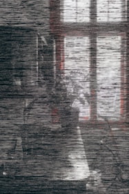 A grainy and distorted image featuring a faint outline of a window casting dim light on a textured surface. The scene is obscured by horizontal noise lines, creating an abstract appearance.